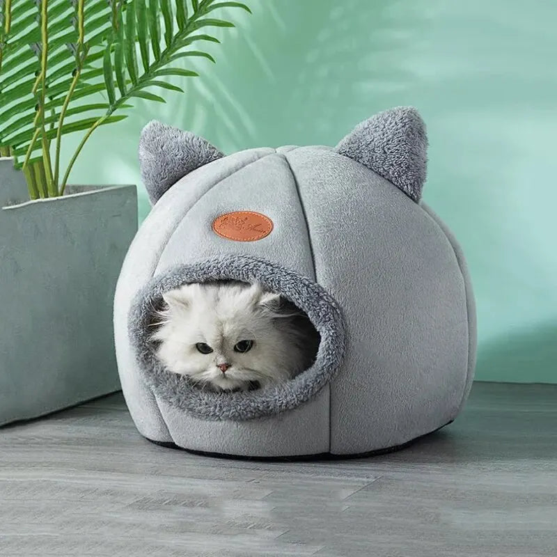 A gray plush cat cave bed with ear shapes and an oval orange patch, featuring a removable cushion.