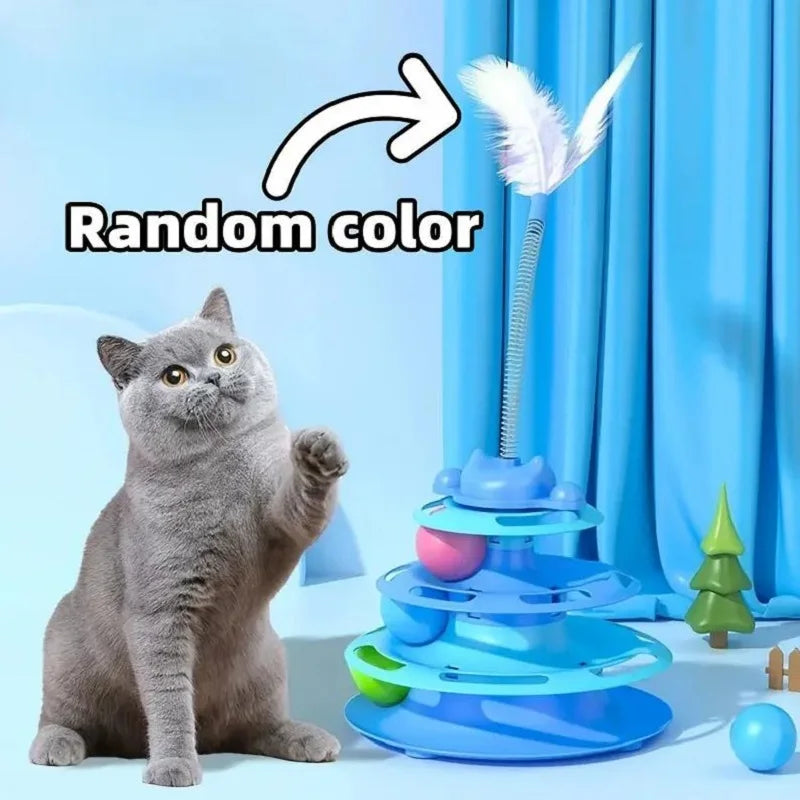 A gray cat sits next to an interactive toy tower with multiple colorful platters and a feather on top.