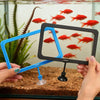 Hands hold a blue feeding ring with a suction cup, positioned above a fish tank filled with red goldfish.