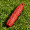 An orange durable EVA chew toy shaped like a elongated cylinder with raised diamond patterns lying on green grass.