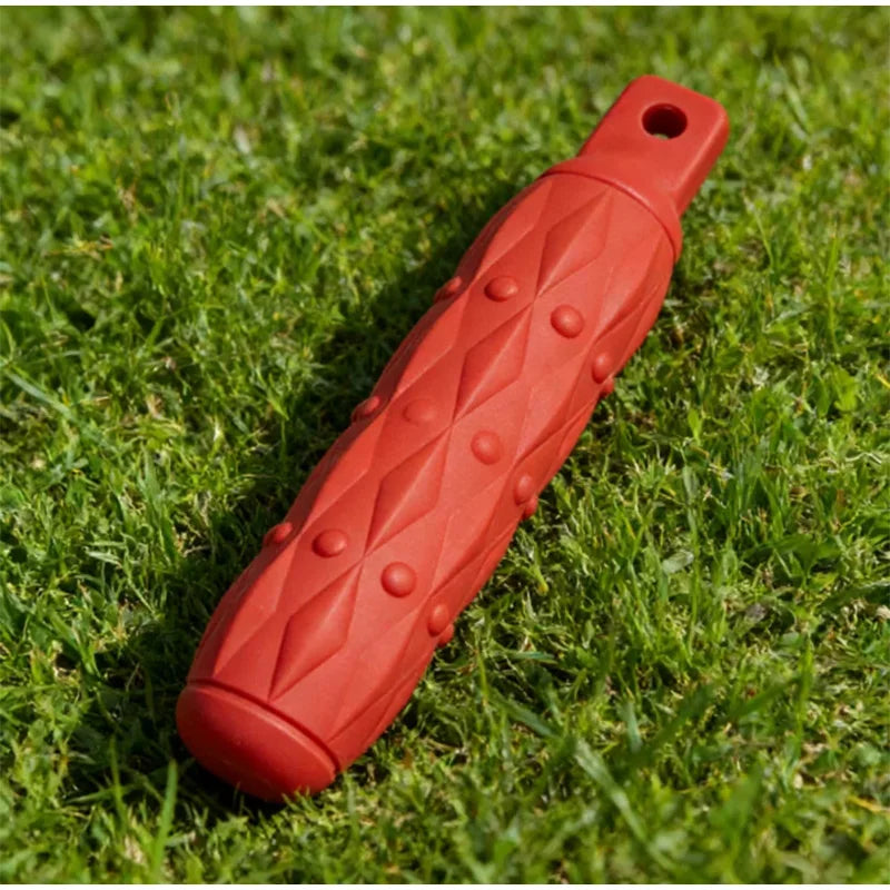 An orange durable EVA chew toy shaped like a elongated cylinder with raised diamond patterns lying on green grass.