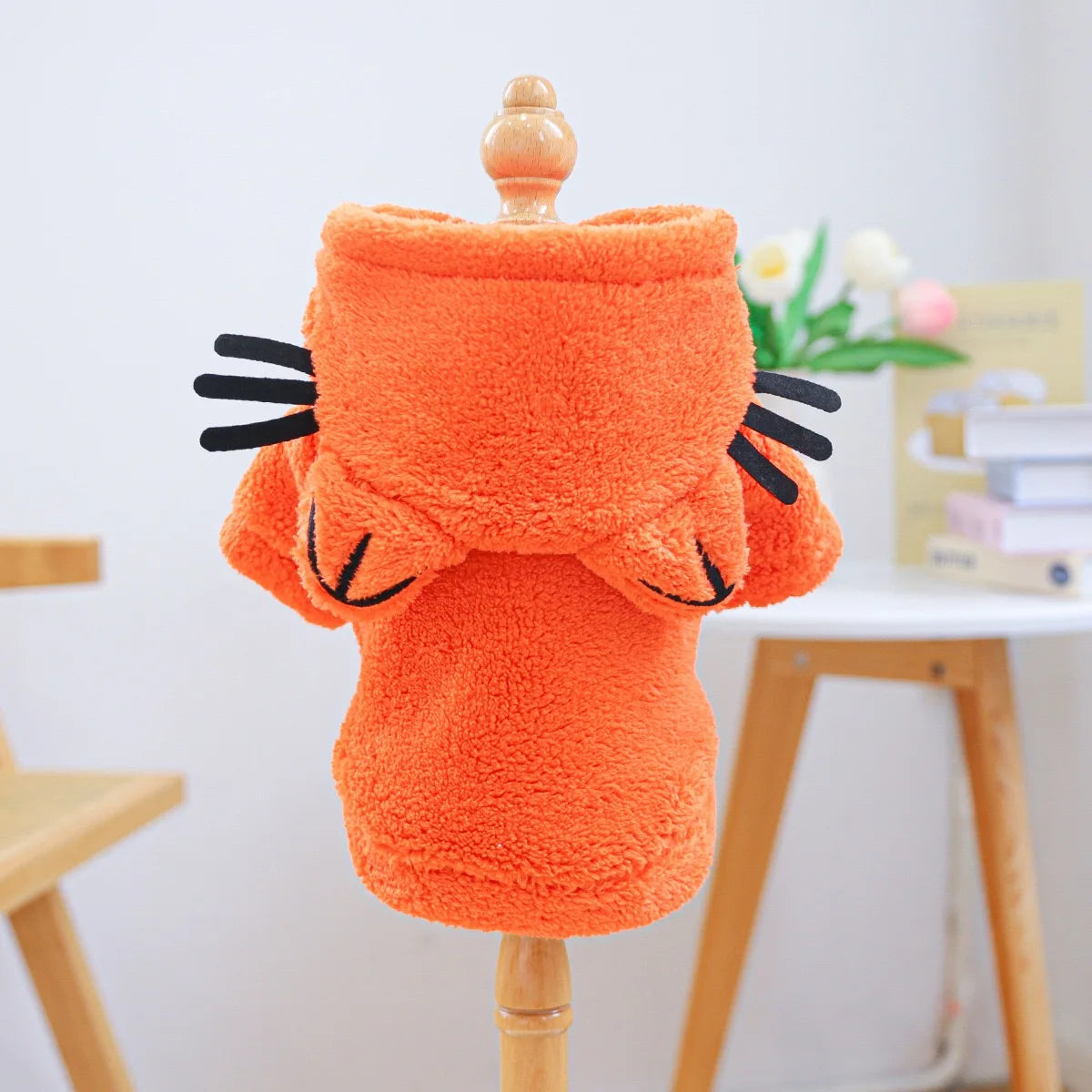 An orange flannel hoodie designed for small dogs, displayed on a wooden stand.