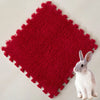 A bright red, textured fleece pet warming mat with a scalloped edge and a small gray rabbit sitting on it.