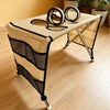 A beige foldable pet grooming hammock with black mesh accents is shown on a wooden floor.
