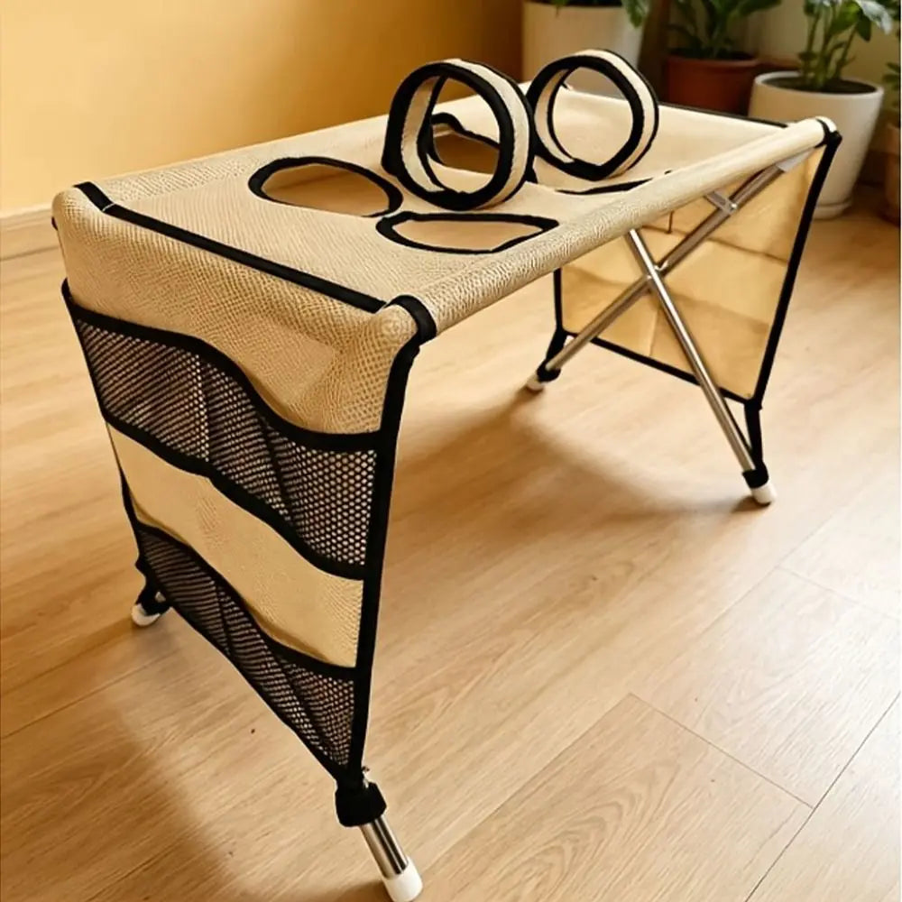 A beige foldable pet grooming hammock with black mesh accents is shown on a wooden floor.