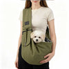 A woman is holding a olive green crossbody pet carrier bag with a black strap and a small white dog.