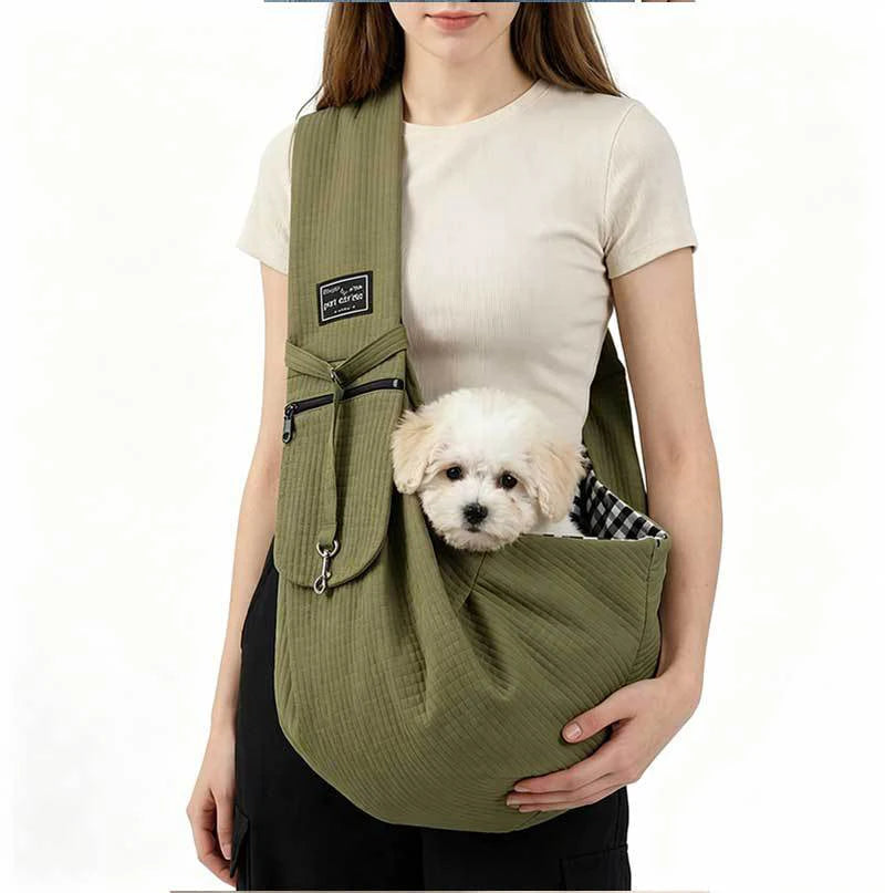 A woman is holding a olive green crossbody pet carrier bag with a black strap and a small white dog.