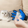 A hand is using a blue silicone pet grooming glove on a gray cat.