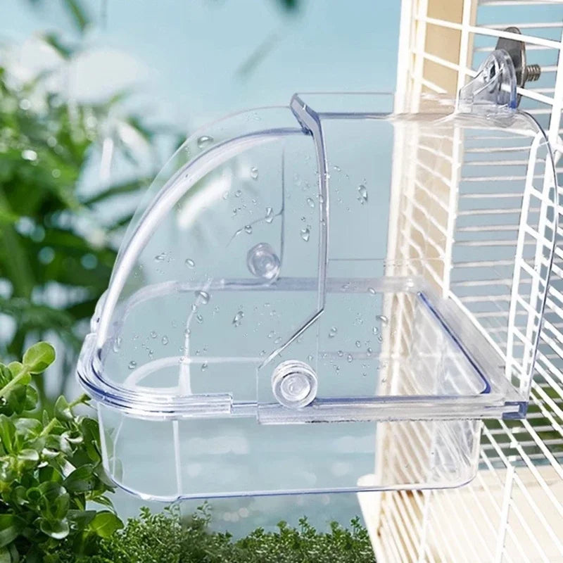 Clear plastic external bird bath designed for cages and parakeets, hanging near foliage.