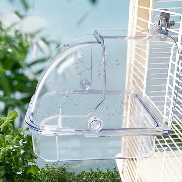 Clear plastic external bird bath designed for cages and parakeets, hanging near foliage.