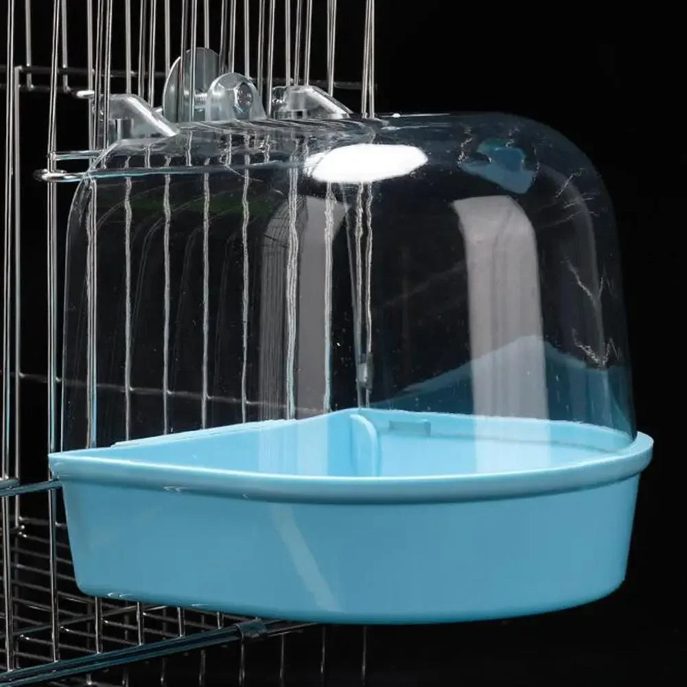 A clear plastic hanging bird bath for parakeets is suspended in a wire cage.