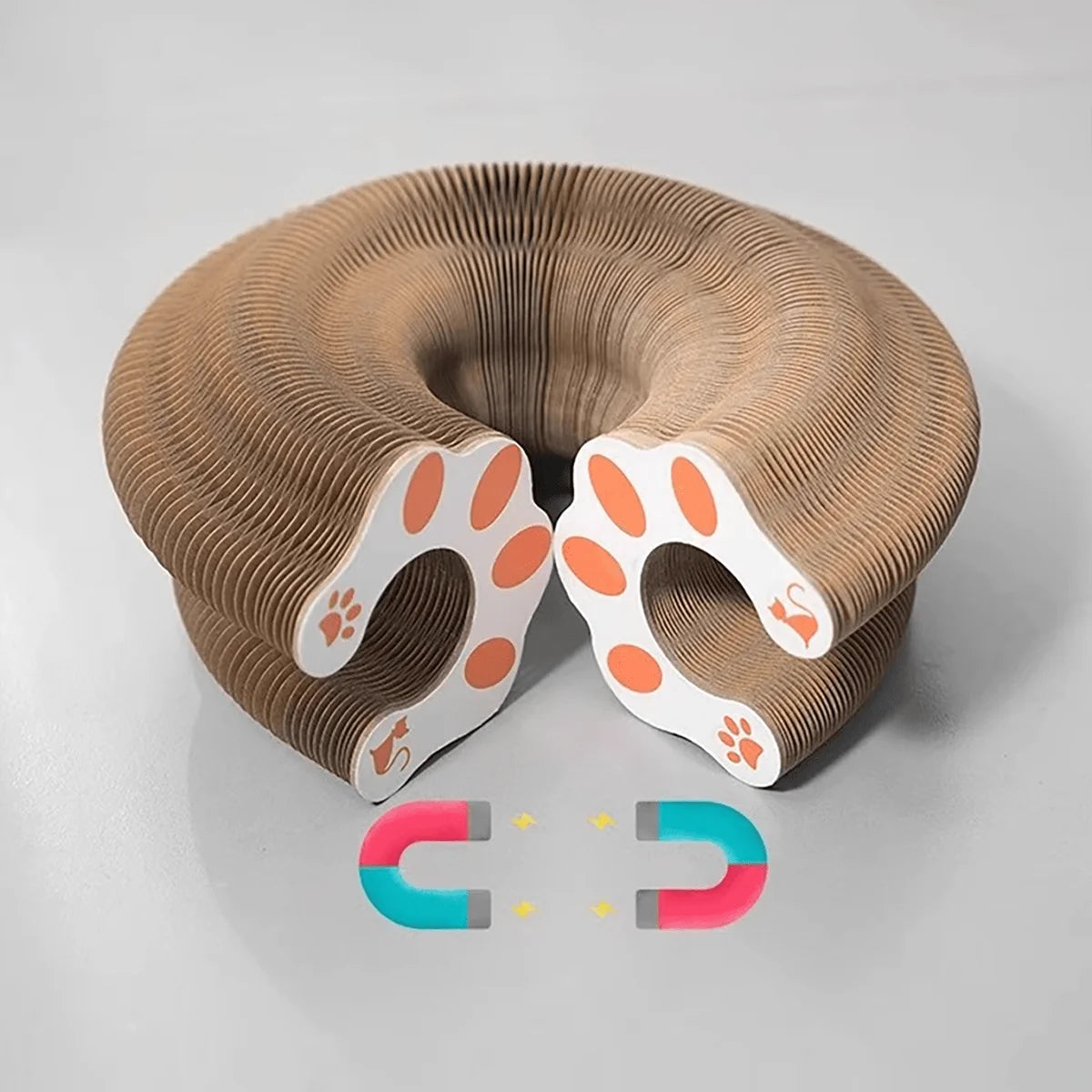 A beige foldable accordion cat scratcher with orange paw shapes and a bell is shown on a gray surface.