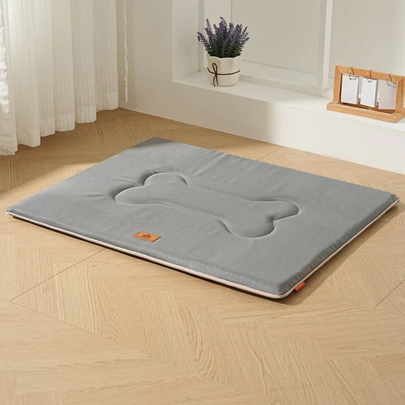 A gray waterproof dog bed mat with a bone shape and cushioned support placed on a light wooden floor.