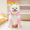 A white dog wearing a pink fleece hoodie with animal ears sitting on a light rug.
