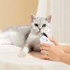 Eine graue Katze sitzt auf einer weißen Oberfläche, während eine Person eine Sicherheitsklemme für Nagelschere hält.