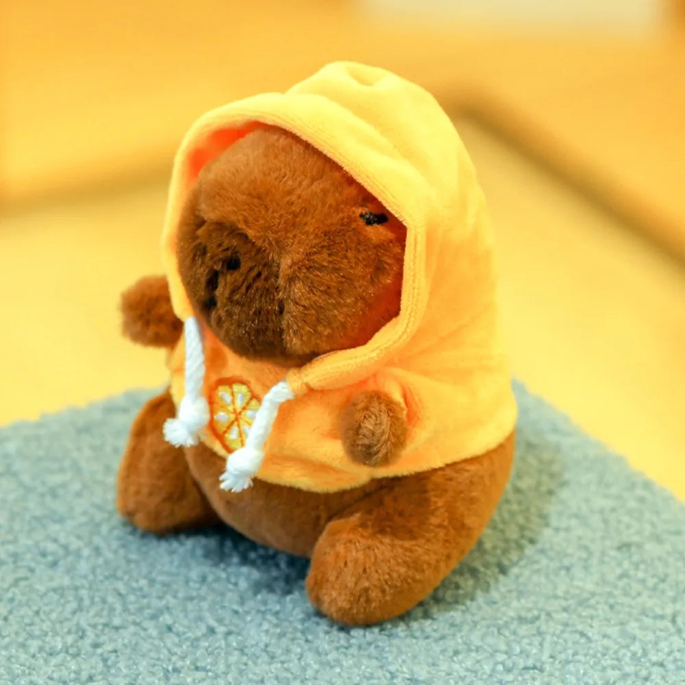 A brown capybara plush doll wearing a yellow hoodie with white trim and small wings.