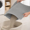 A hand is pouring light gray cat litter from an extra-large double-layer honeycomb texture mat into a white bowl.