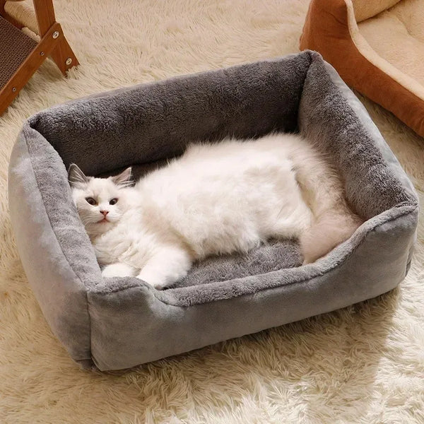 A fluffy white cat is relaxing inside a gray plush cat bed on a light-colored rug.