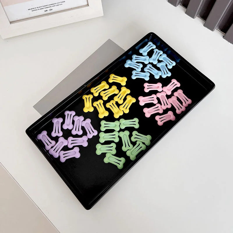 A black tray holds various bone-shaped hair clips in pastel colors for pet grooming.