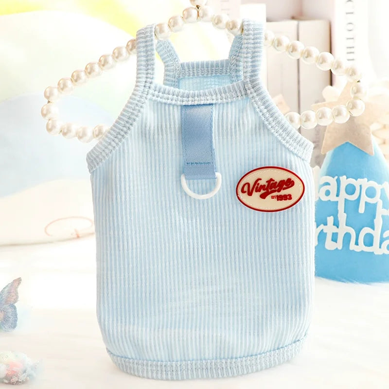 Light blue striped dog vest with a vintage tag and pearl necklace displayed on a white surface.