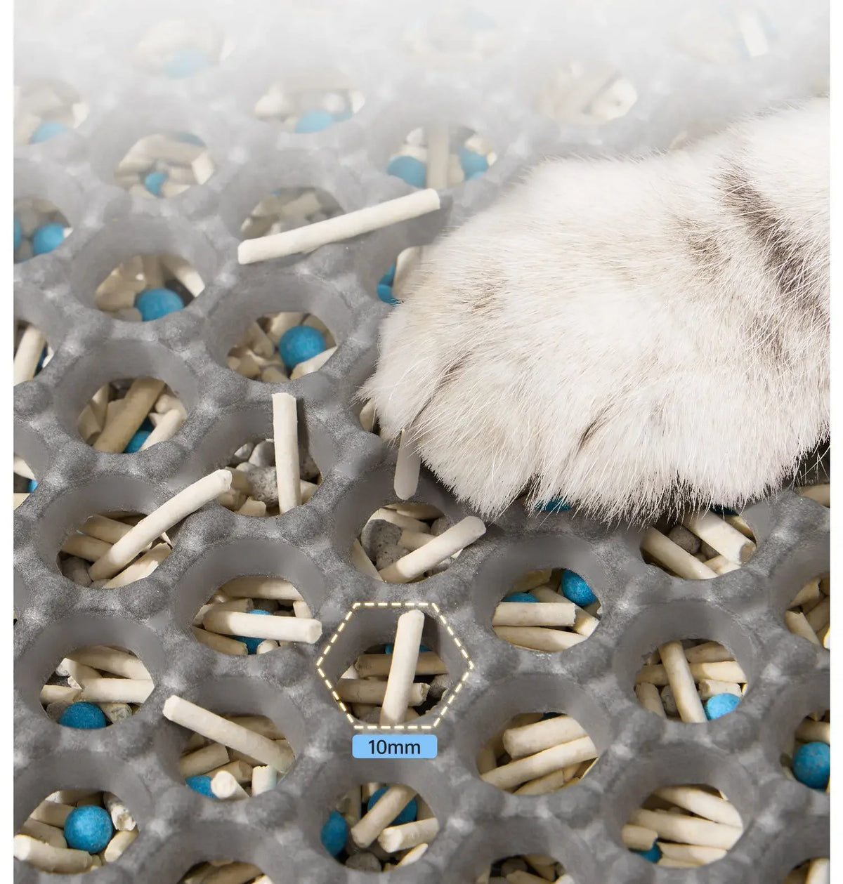 A white cat paw rests on a honeycomb litter mat filled with small, light-colored pellets and blue accents.