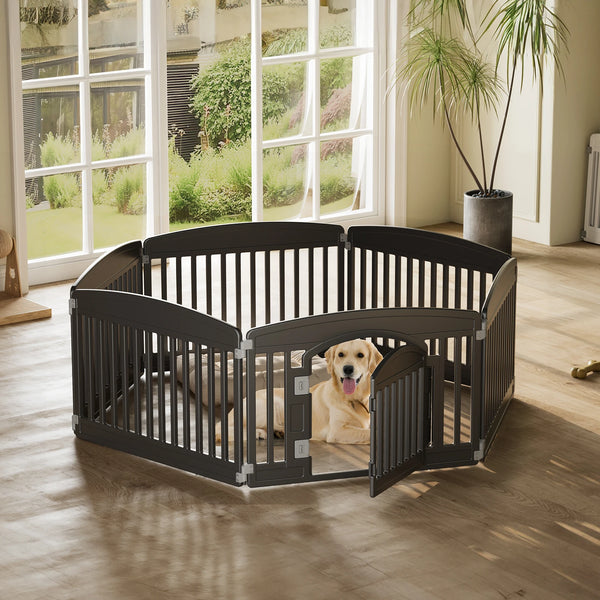 A black expandable plastic dog playpen with a curved design sits on a wooden floor near a large window.