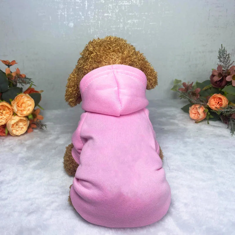 A pink knitted hoodie for a dog with brown fuzzy ears, displayed on a light surface.