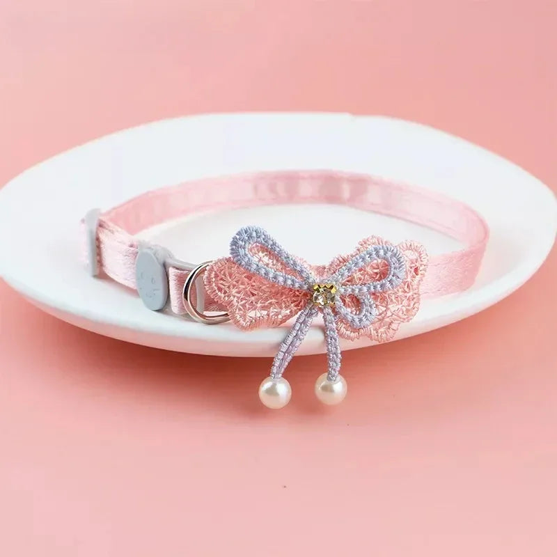 Pinkes Spitzen-Tierhalter mit Schleife und hängenden Perlen auf weißem Teller.