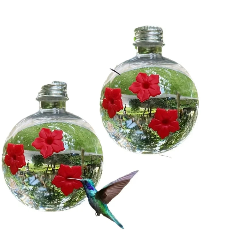 Un distributeur d'eau sphérique en verre rempli d'eau et de fleurs, à côté d'un colibri.