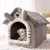 A gray dog house pet bed with a felt roof and an arched entrance, featuring a small white puppy inside.