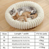 A round, white pet bed with a plush bolster support is shown, containing three small cats.