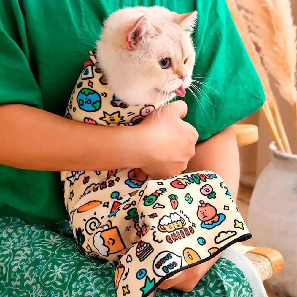 A person is holding a small white cat wrapped in a patterned fabric pet swaddle.