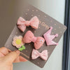 Una mano sostiene una tarjeta con cinco lazos de tela hechos a mano rosa y morado para clips de pelo de mascotas.