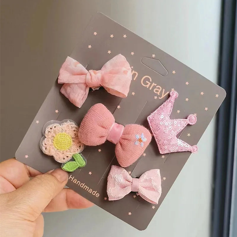 Una mano sostiene una tarjeta con cinco lazos de tela hechos a mano rosa y morado para clips de pelo de mascotas.