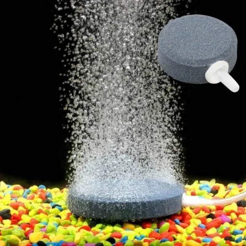 A grey air stone disc is shown spraying fine bubbles onto a colorful surface.