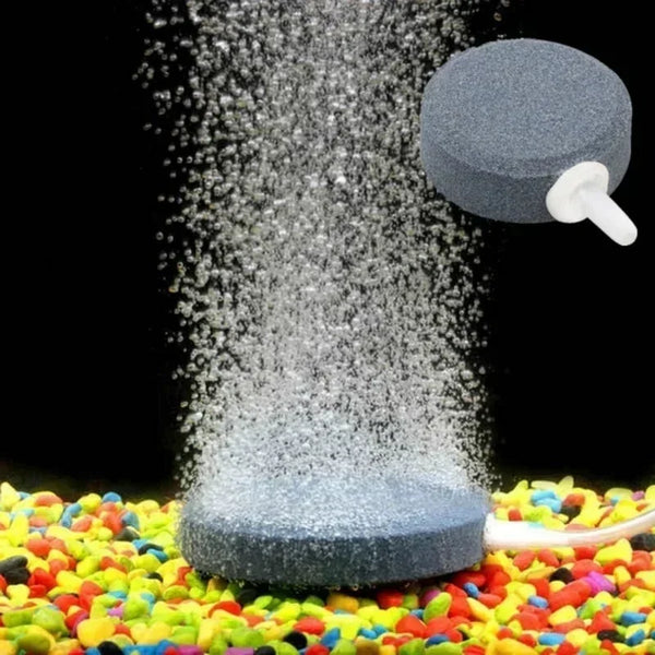 A grey air stone disc is shown spraying fine bubbles onto a colorful surface.