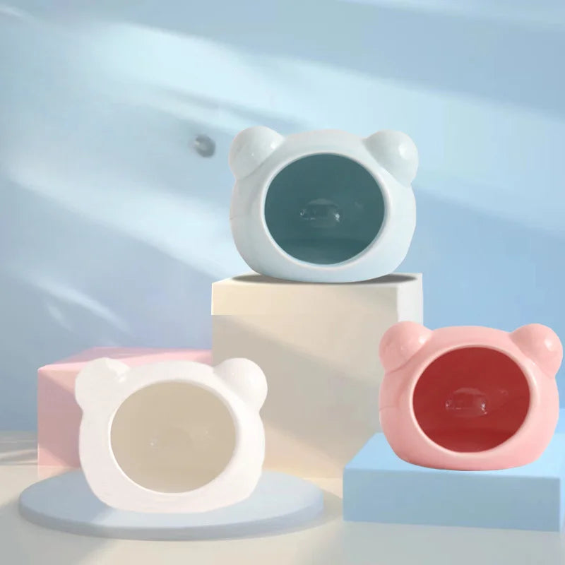 A white ceramic hamster house with a cooling design is shown alongside a pink version on a light blue surface.
