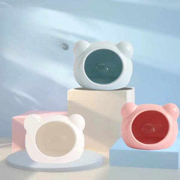 A white ceramic hamster house with a cooling design is shown alongside a pink version on a light blue surface.