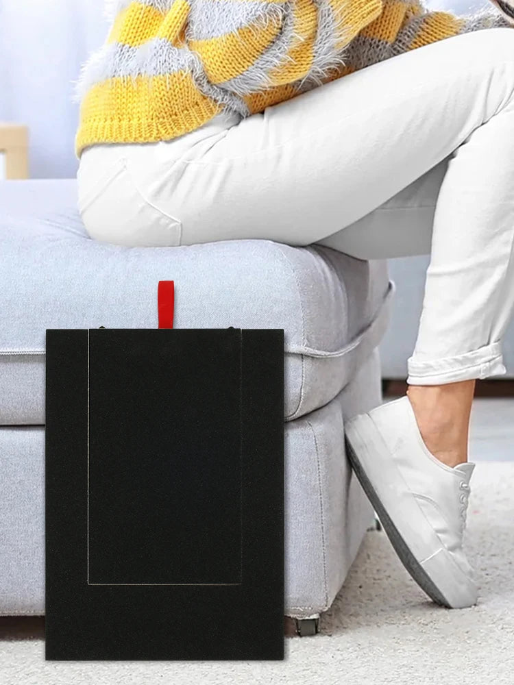 Schwarzes Holz-Nagelfil-Board mit rechteckiger Öffnung auf einem hellgrauen Sofa neben einem Bein.