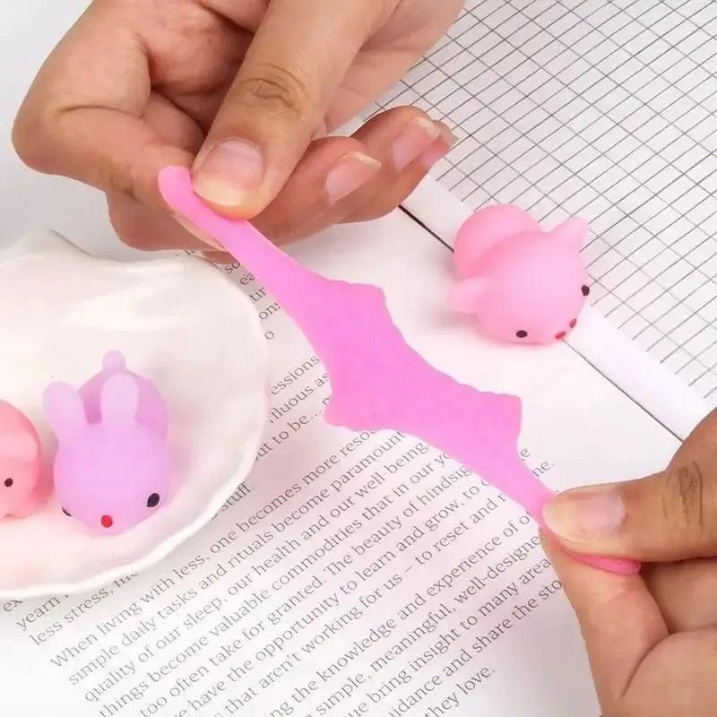 A hand is squeezing a pink, adorable animal stress relief toy onto graph paper.