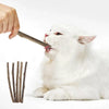 A white cat is licking a natural herbal cat chew stick held by a human hand.