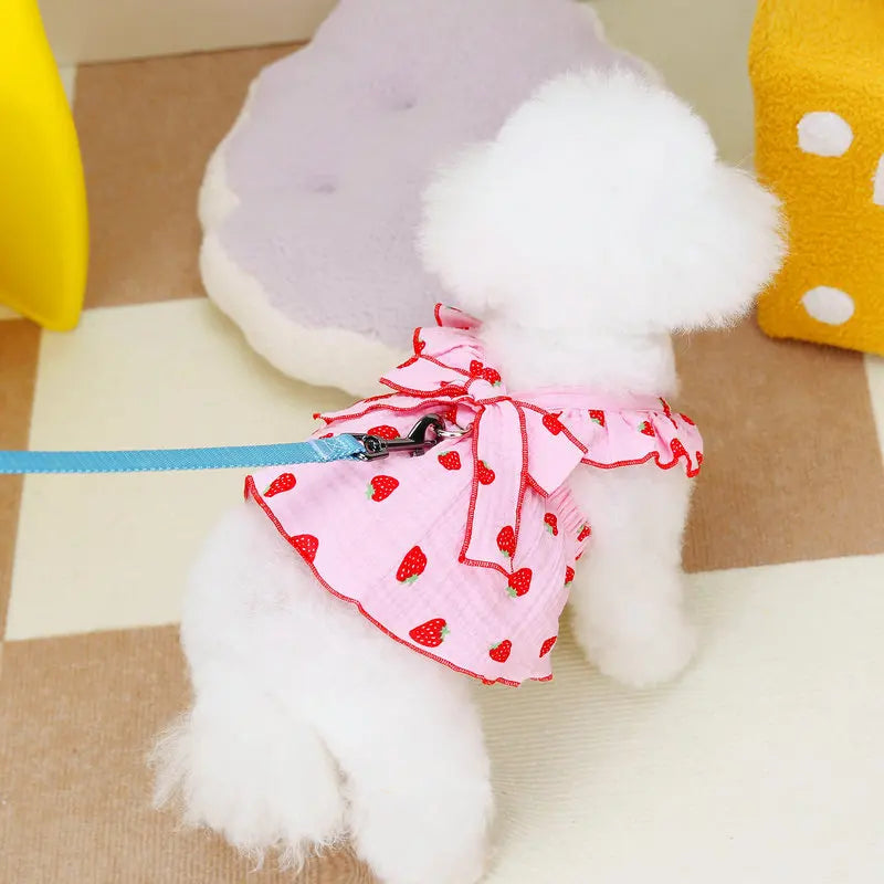 A fluffy white dog plush toy wearing a pink strawberry patterned dress and blue ribbon.