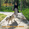 A woman is walking two large white dogs on a leash outdoors on a paved path.