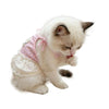 A small white kitten wearing a pink floral print dress with thin straps.