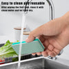 A hand is rinsing a teal fish tank cleaning brush under running water in a kitchen sink.