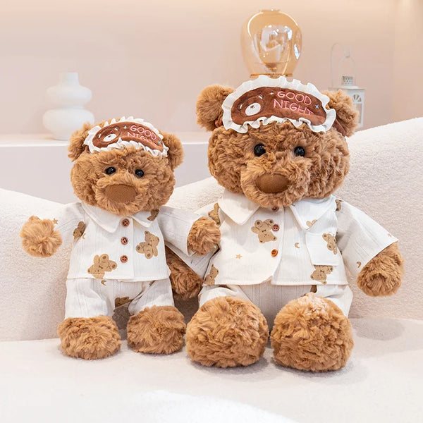 A fluffy teddy bear wearing pajamas with a good night headband and an eye mask.