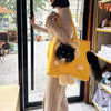 A person is holding a yellow breathable mesh pet carrier backpack with a fluffy cat inside, standing in a shop or market sett