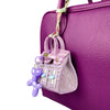 A handcrafted mini house-shaped bag in light purple with a puppy keychain charm hanging from the strap.