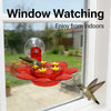 A red hummingbird feeder with a suction cup and hanging hook is visible through a window.