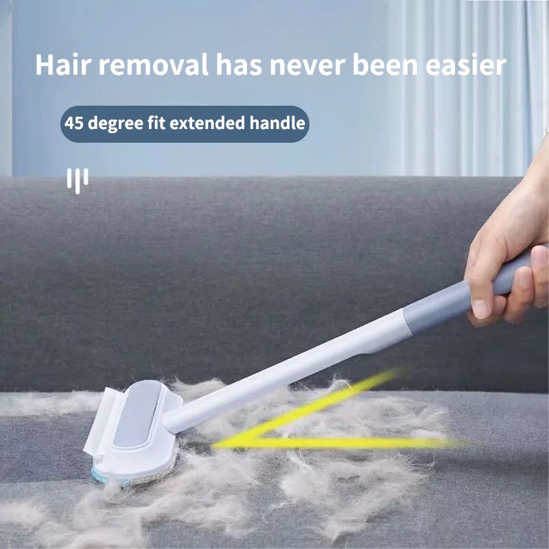 A hand is using a white pet hair remover brush with an extended handle to remove pet hair from a gray surface.